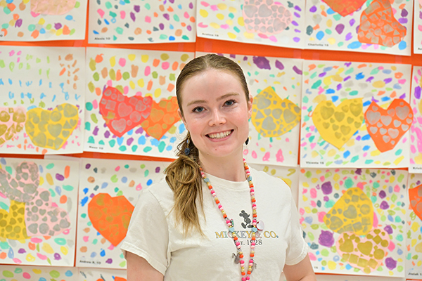 A woman smiles in front of a wall of student artwork