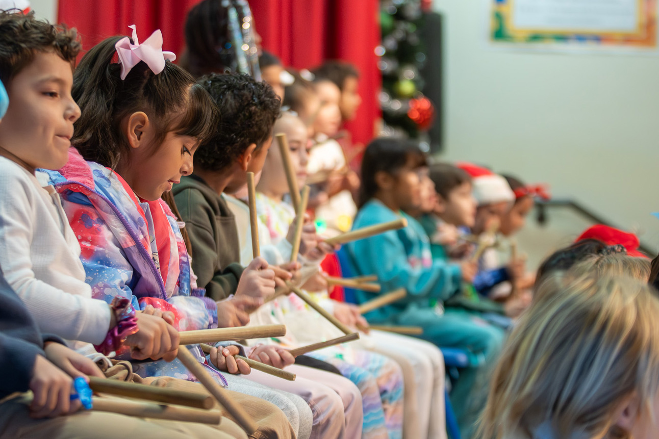 Child kneels and drums on a tube with drumsticks