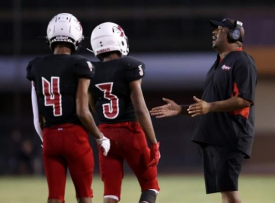 New Santa Rita head football coach Douglas Smith talks on the field with two players.