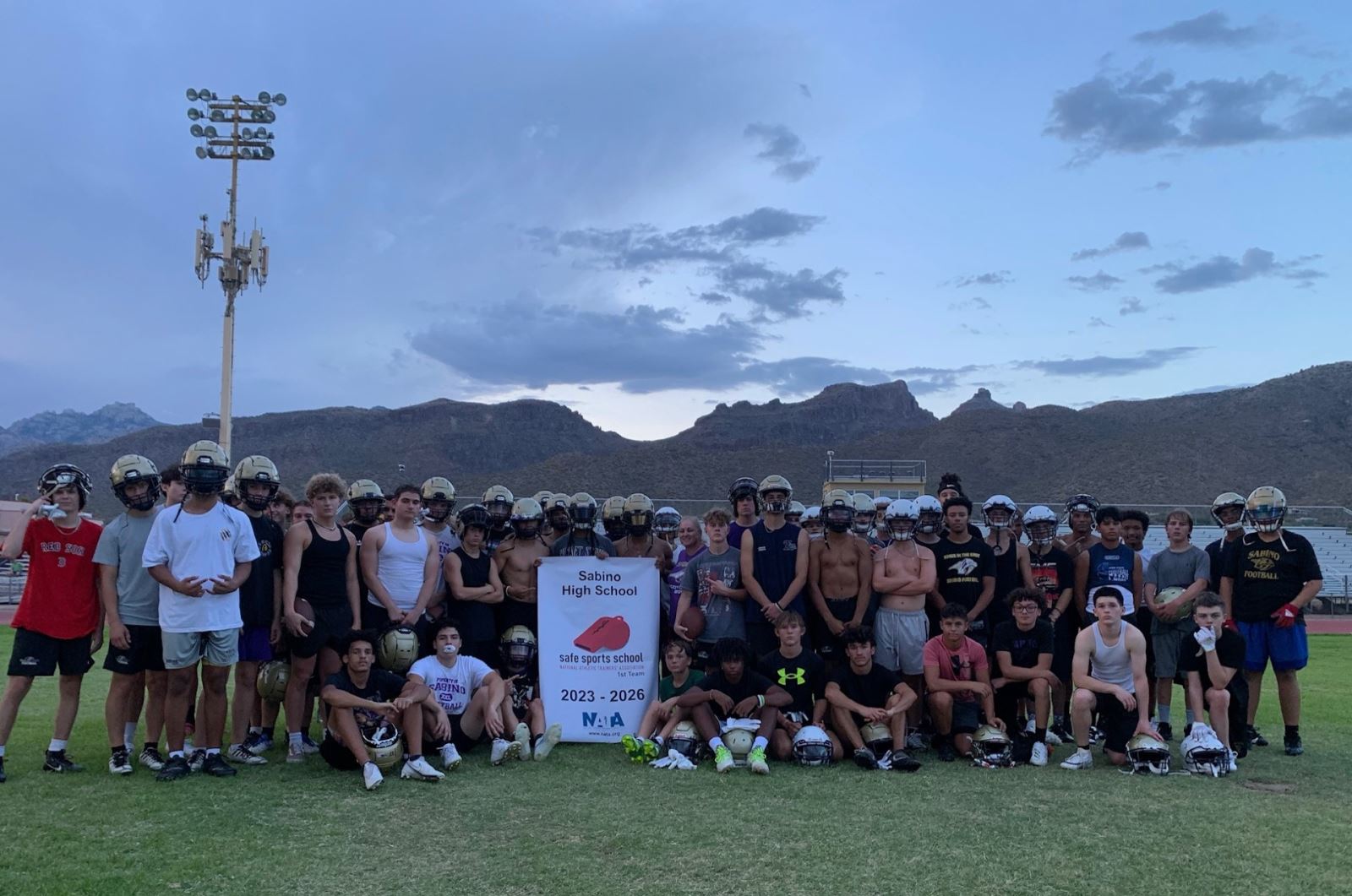 The Sabino High School football team holds up the school's Safe Sports School Award banner on the football field.