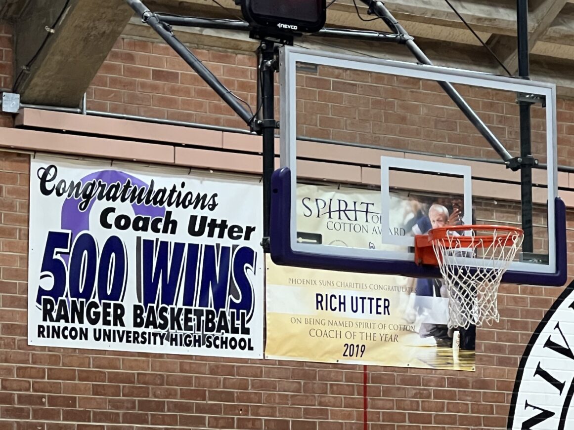 A banner reading Congratuations Coach Utter 500 Wins Ranger Basketball Rincon University High School hangs behind the basketball hoop