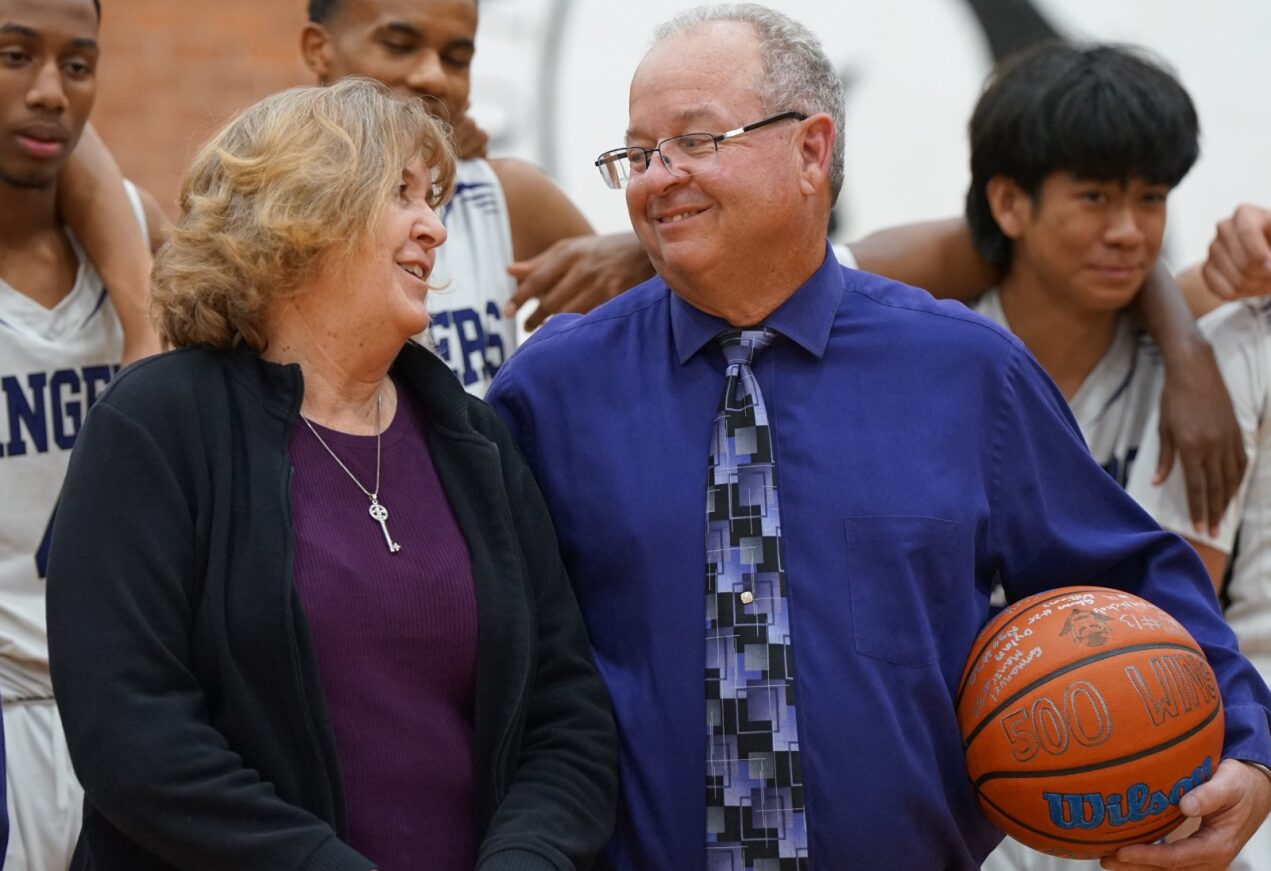 RUHS Coach Utter smiles next to his wife while holding a basketball