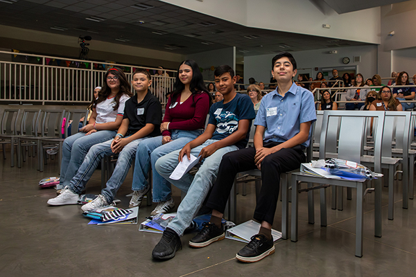Students smile in their seats in the auditorium during the symposium
