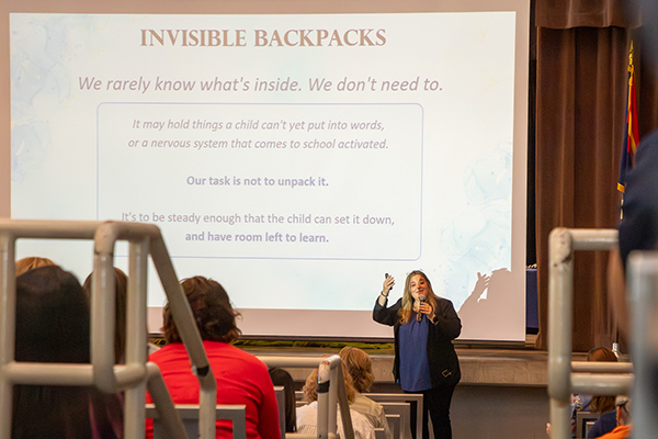 A woman talks to the audience in front of a Powerpoint screen