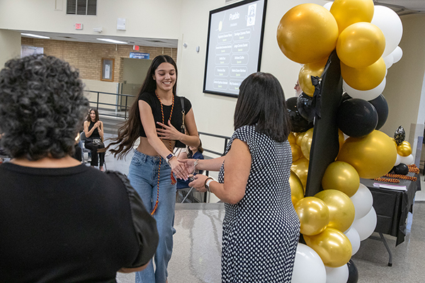 A teen girl excitedly shakes hands on stage after getting her biliteracy cord