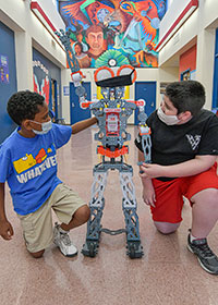 Two children kneeling beside a robot.