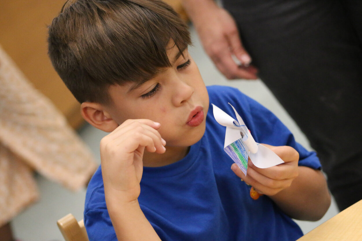 A boy blows on a paper pinwheel he made.