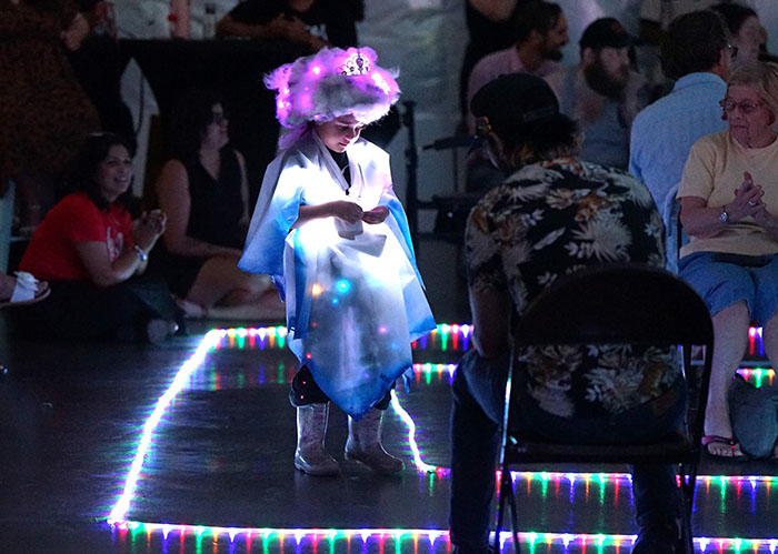 A girl in a light-up white dress walks the runway
