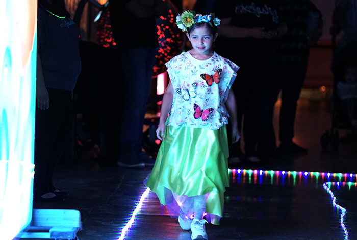 A girl in a light-up costume with butterflies on it walks the runway