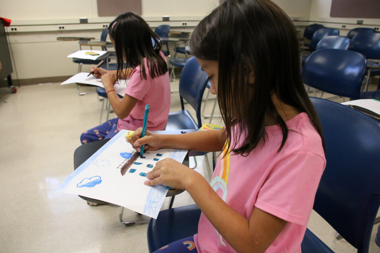 Two young girls in pink shirts work on drawings during ¡Adelante!