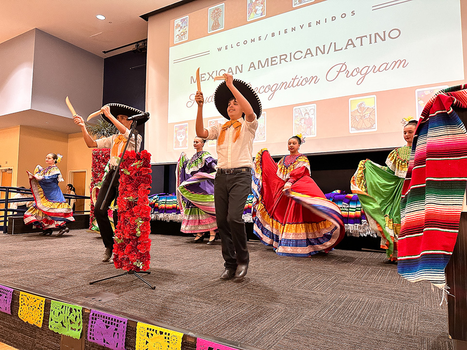 Student folklorico performers dance on stage in colorful outfits