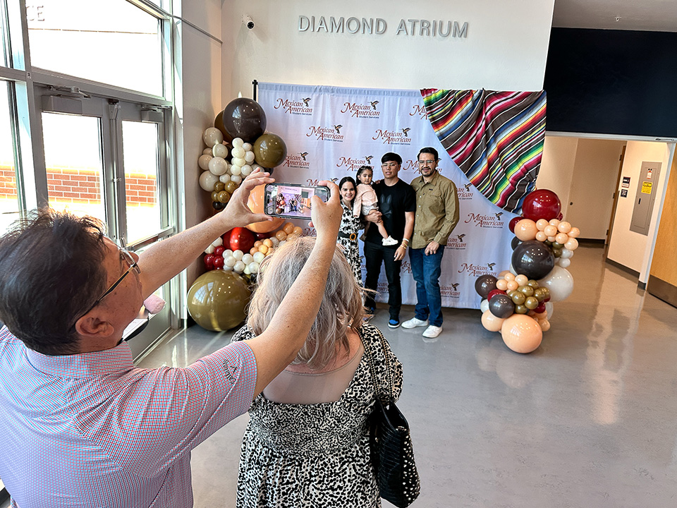 A man takes a photo with his phone of a family, over the head of a woman