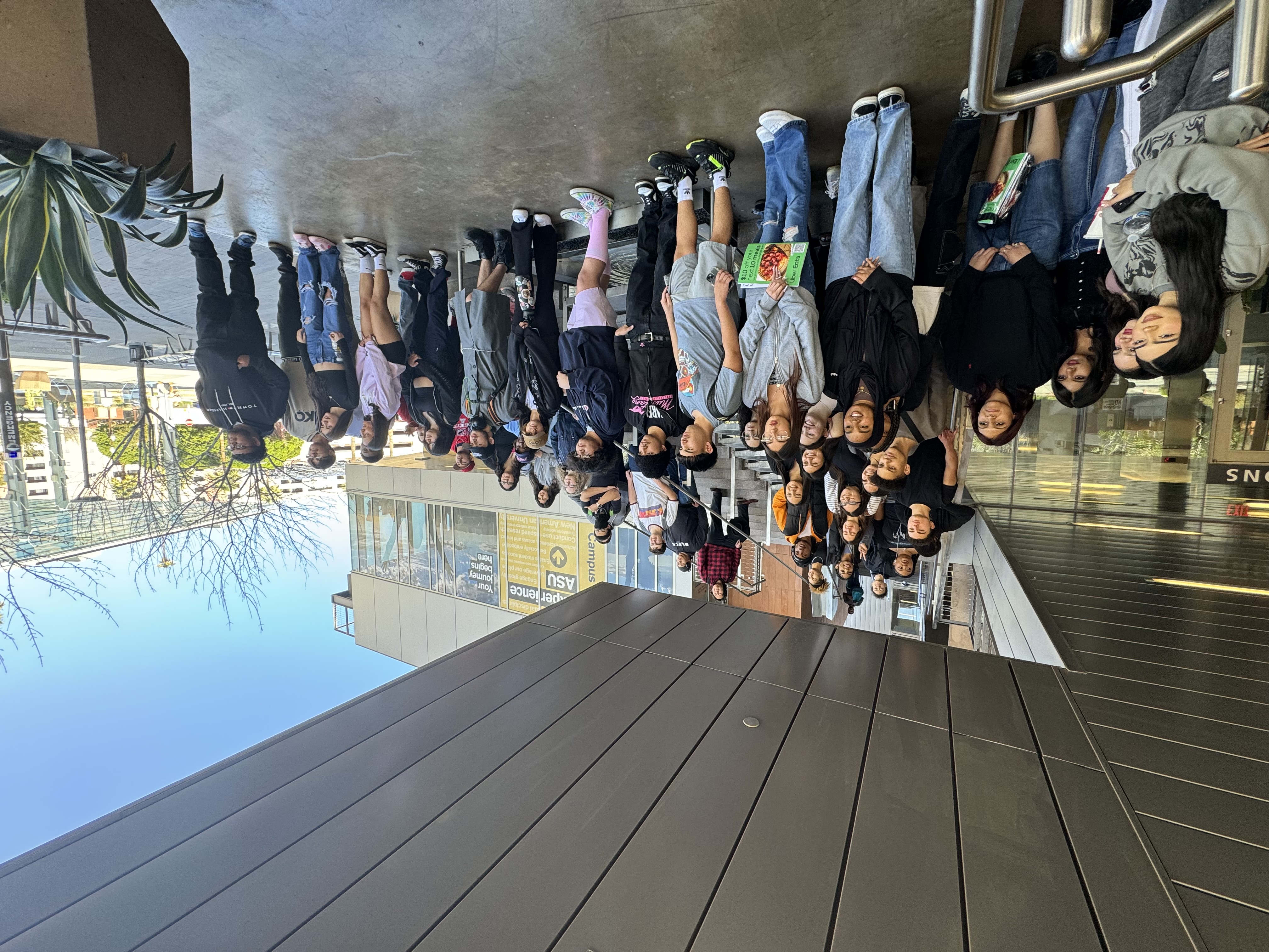 A woman with long dark hair wearing a red shirt addresses a crowd