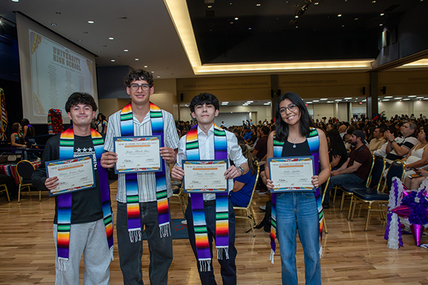 Four high school students proudly show off their award certificates in the auditorium