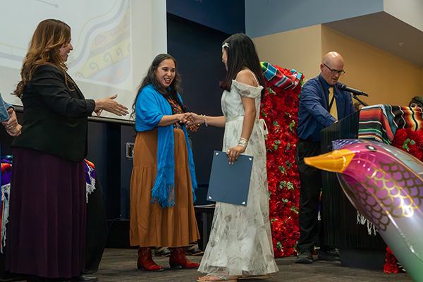 Two women congratulate a teen girl as she accepts her award certificate