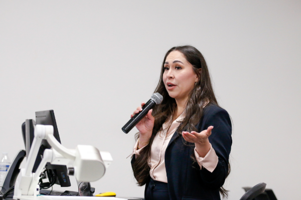 A woman with dark hair wearing a black pantsuit talks to the audience in a microphone
