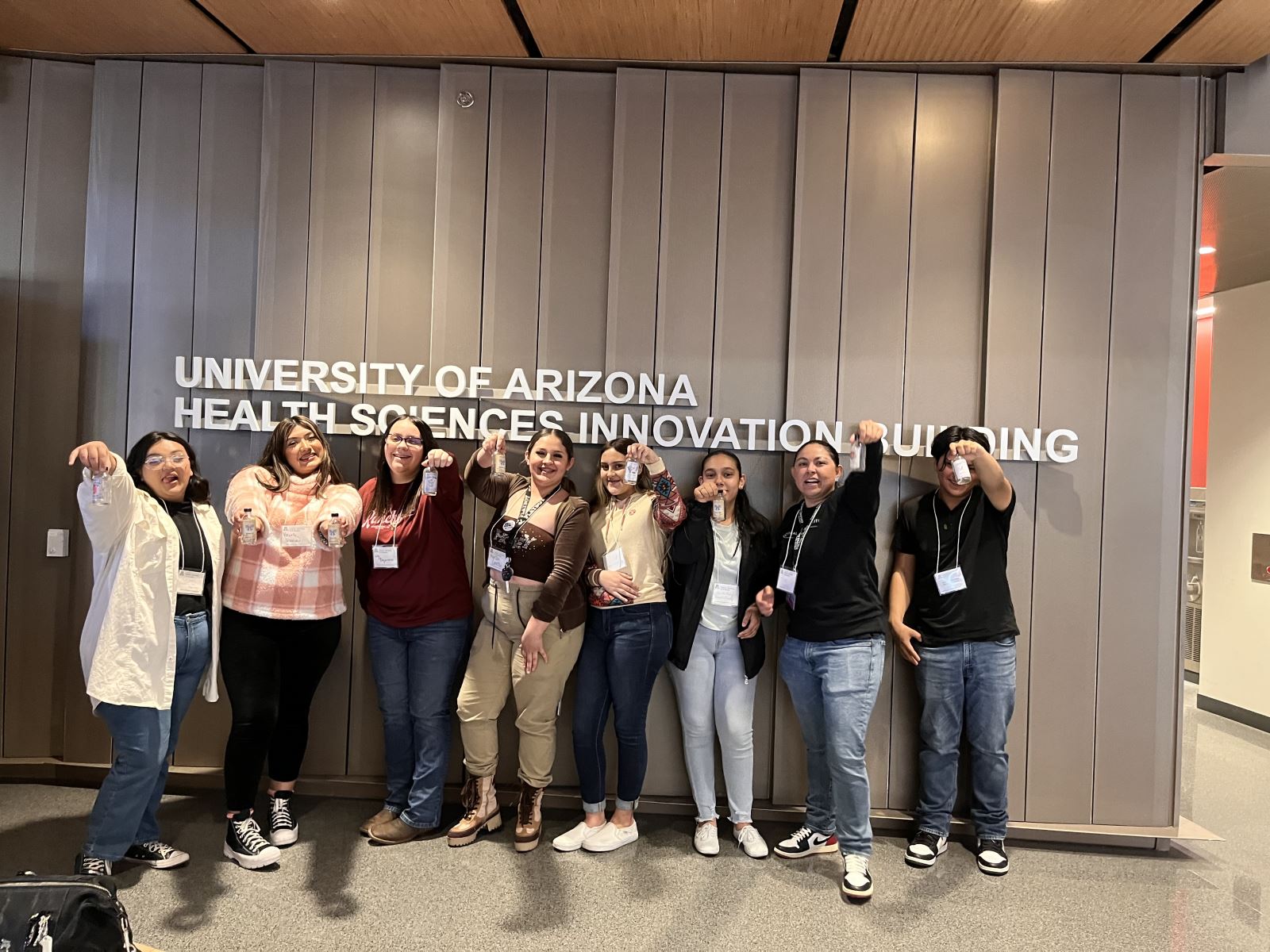 Students holding up bottles in front of University of Arizona Health Sciences and Innovation Building sign. 