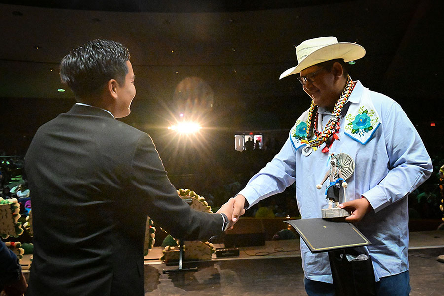 A teen boy in a cowboy hat shakes a man's hand