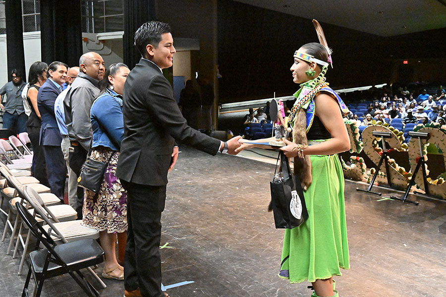 A teen girl wearing a feather headband shakes a man's hand
