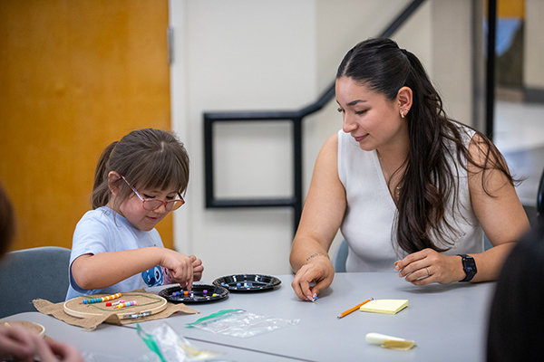 A woman helps a little girl put beads on a round board