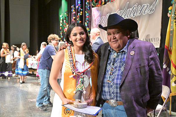 A teen girl poses with her award next to a man in a cowboy hat