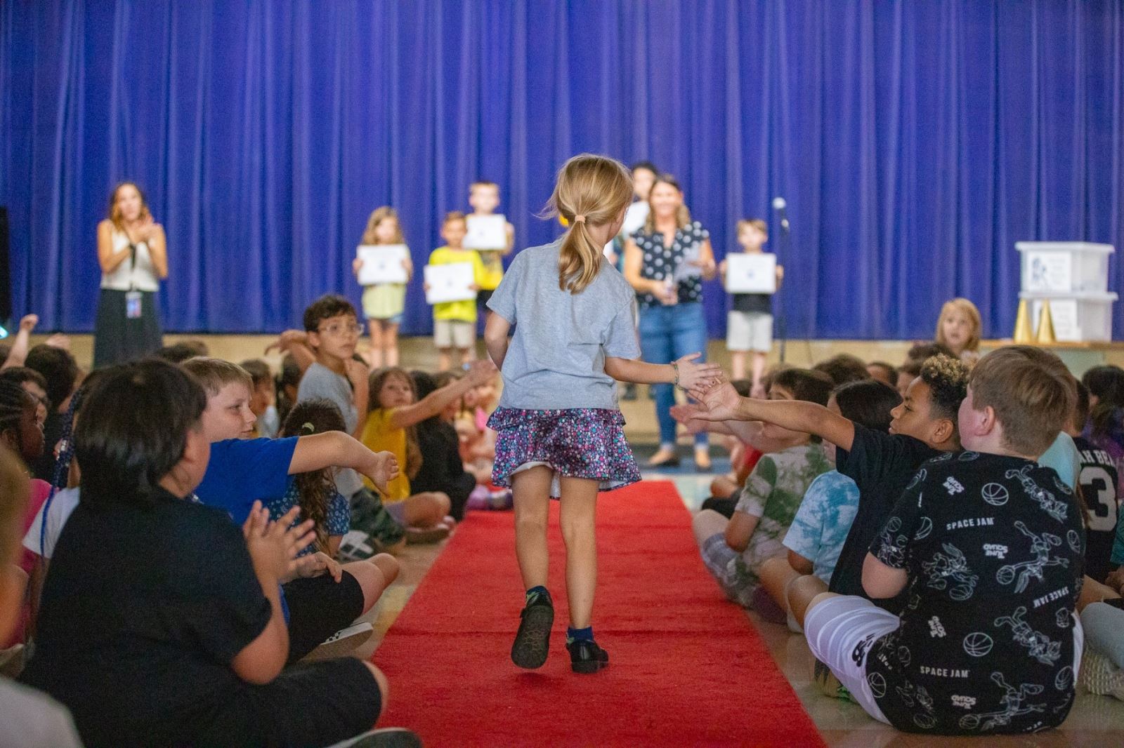 A young girl gives out high fives as she walks down the red carpet at the assembly.