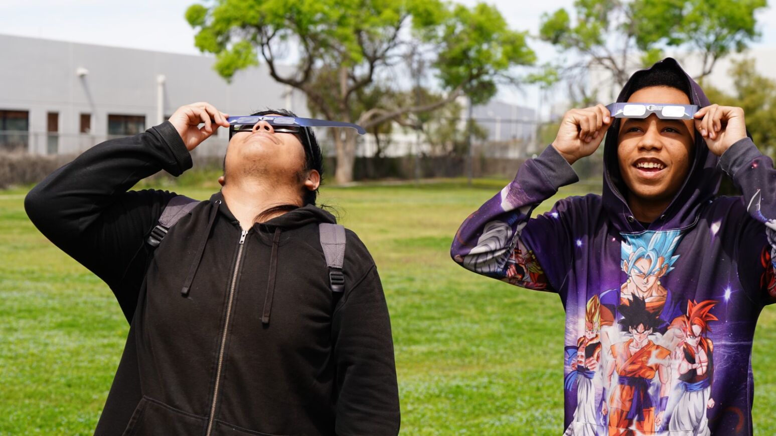 Two teen boys look up at the eclipse with their special glasses