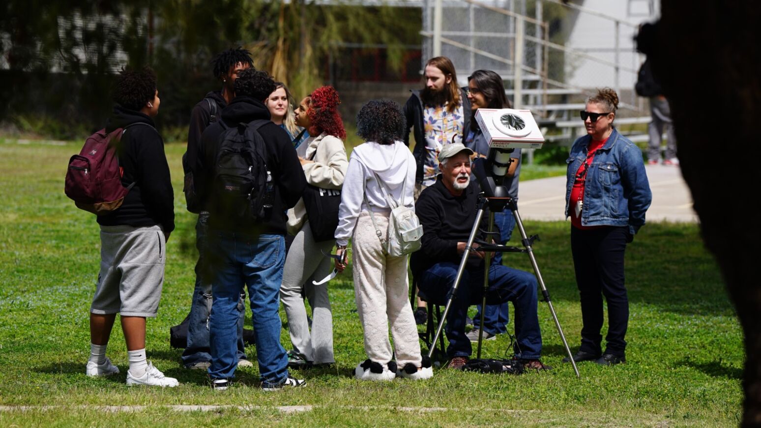 A group of students stand around outside waiting to look at the eclipse