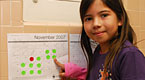 Young girl with dark hair points to a calendar in a classroom.
