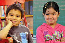 Young boy in a gray t-shirt and young girl in a pink sweatshirt smile in a classroom.