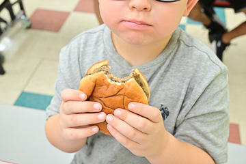 Child eats a hamburger as big as his face.