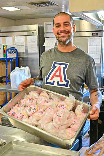 Staff shows tray of baked goods with sprinkles ready to serve.