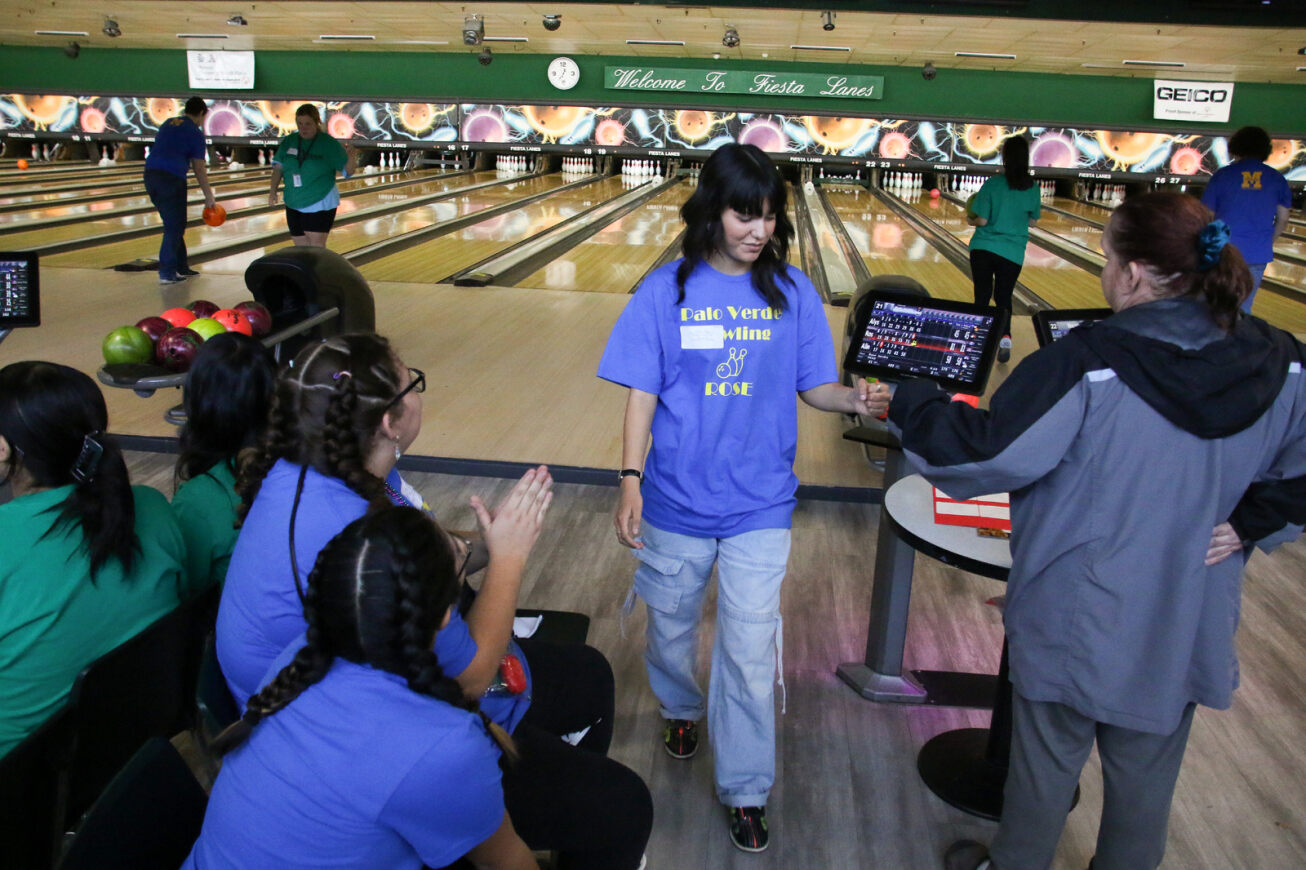 A girl in a blue shirt gives a fist bump to a teammate after bowling her frame.