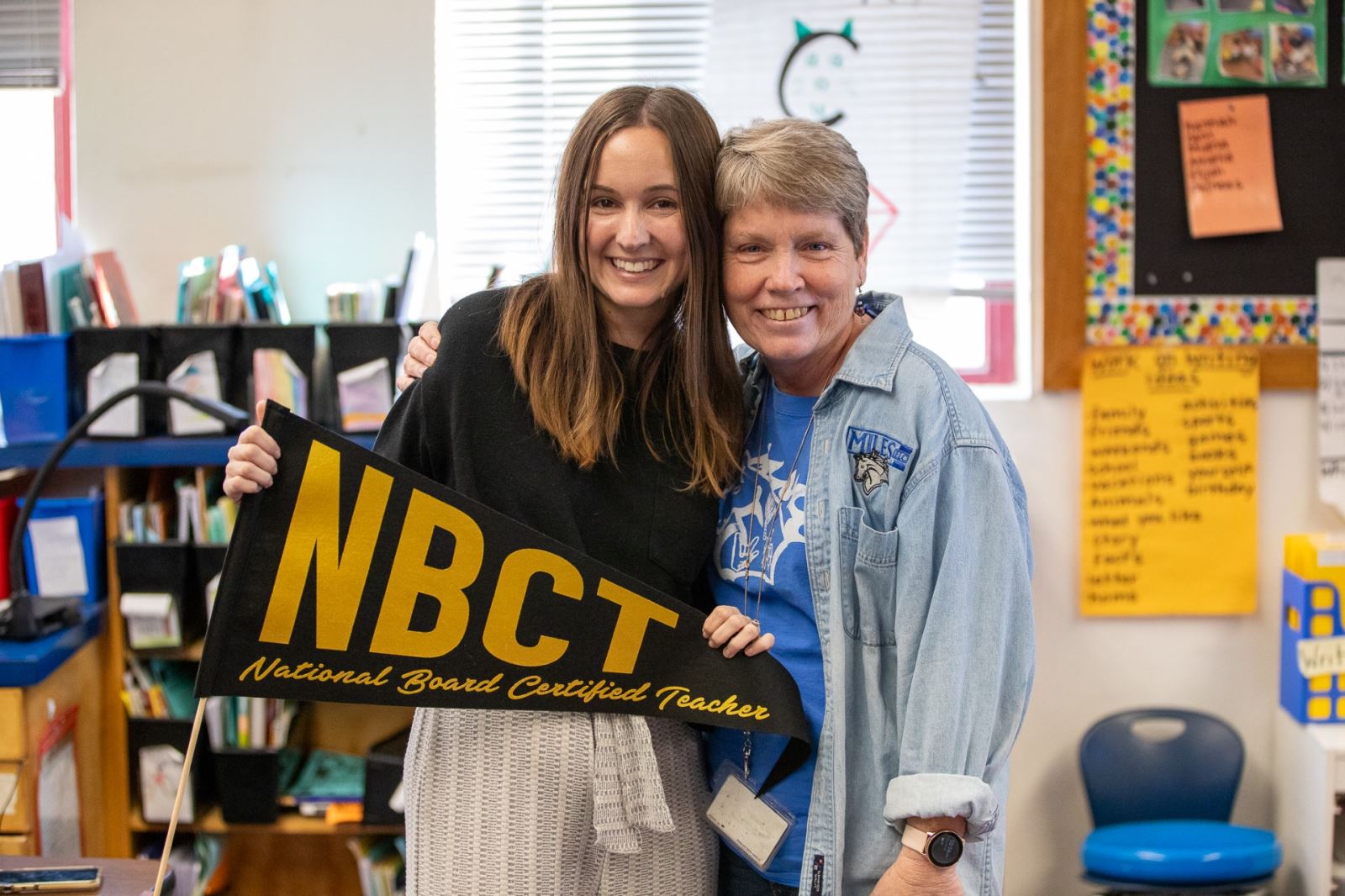 Erin Hines smiles next to her aunt, Patty, while holding an NBCT pennant.