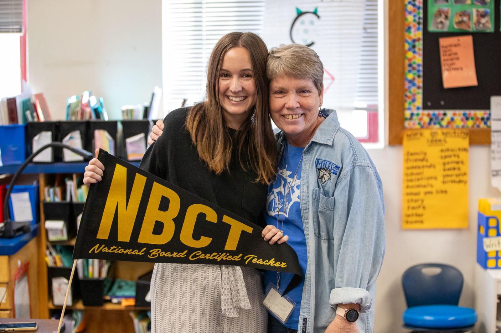Erin Hines smiles next to her aunt, Patty, while holding an NBCT pennant.