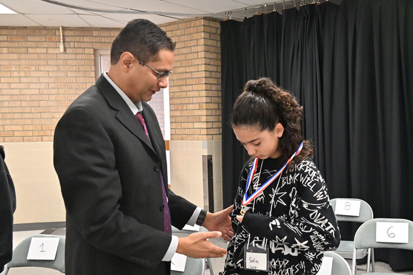Governing Board member Dr. Ravi Shah places the third place speller's medal around her neck.
