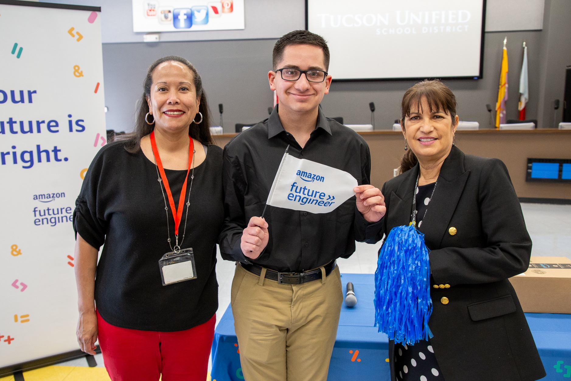 Tucson High senior Anthony Talavera smiles and poses with an Amazon Future Engineer flag and two TUSD staff members