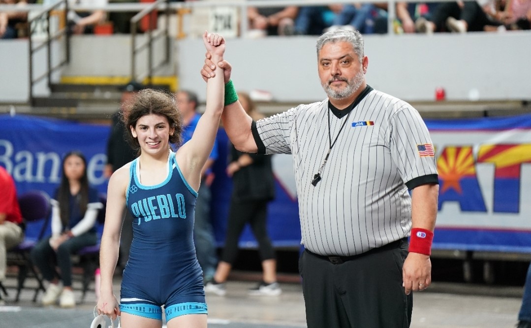 Elizabeth Valenzuela-Smith smiles with her arm held up by an AIA official after winning a tournament