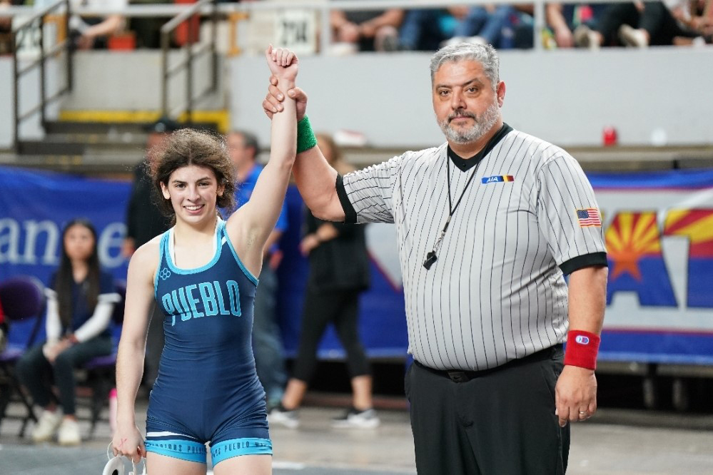 Elizabeth Valenzuela-Smith smiles with her arm held up by an AIA official after winning a tournament