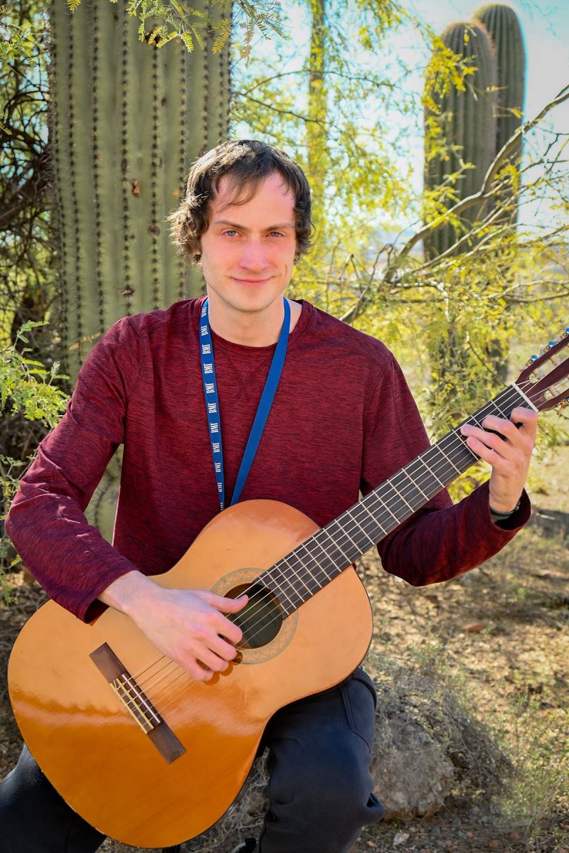 John Ensey poses with a guitar in front of a saguaro.