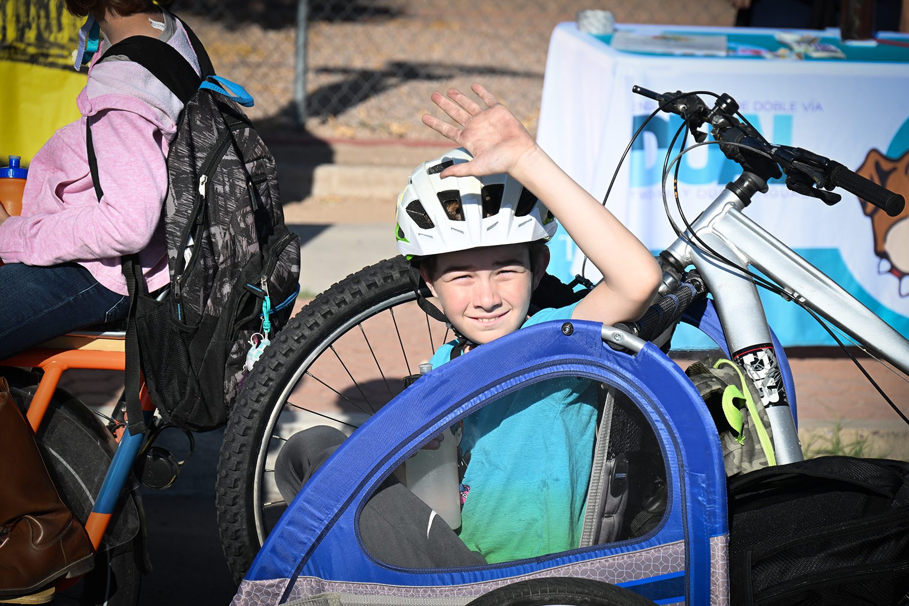 A boy in a bike helmet waves from his bike cart