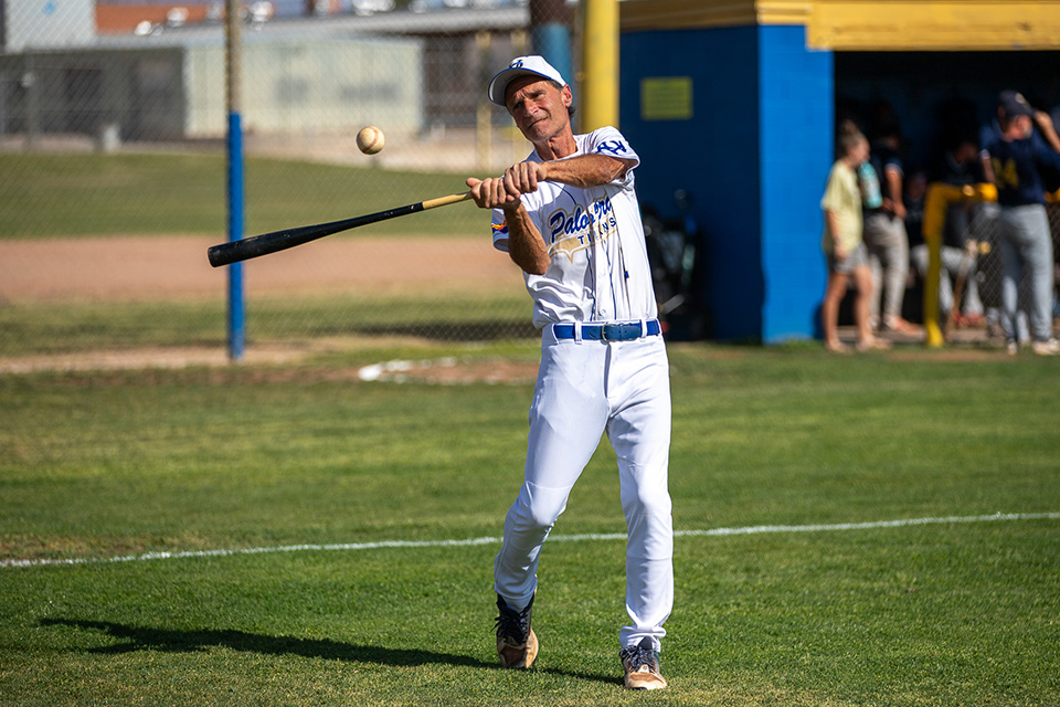 A man in a white baseball jersey swings the bat at the ball