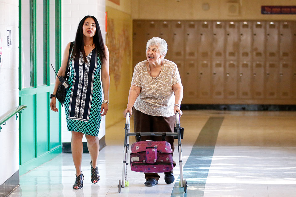 Roberts-Naylor's principal walks down the hall with an older woman using a walker
