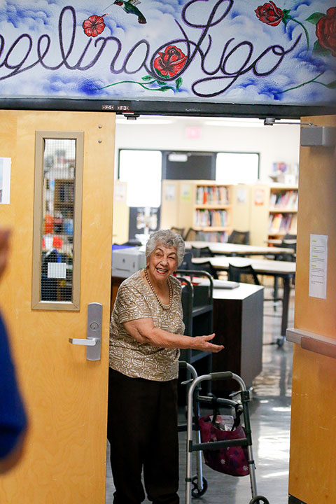 A woman with a walker smiles as she invites guests into the library