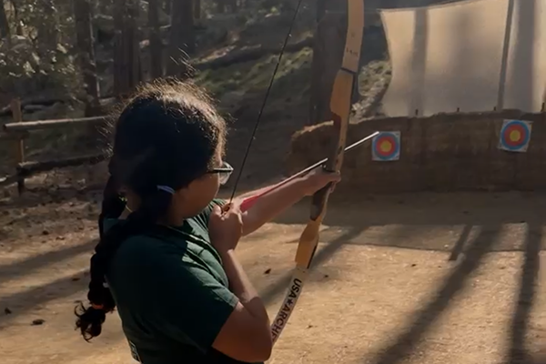 A girl aims a bow and arrow at a target