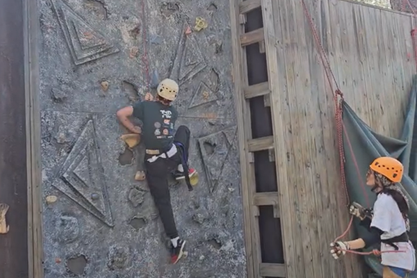 A boy climbs a rock wall attached to a rope