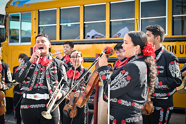 High school mariachi musicians perform in front of an EV school bus