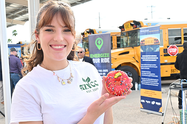 A woman holds up a donut decorated with a school bus trinket