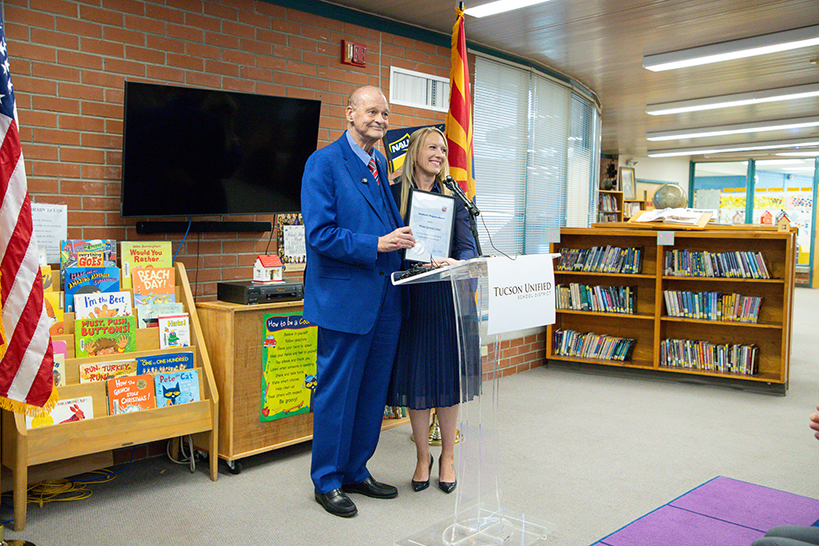A man in a blue suit and a woman in a blue dress hold an award certificate behind a clear podium