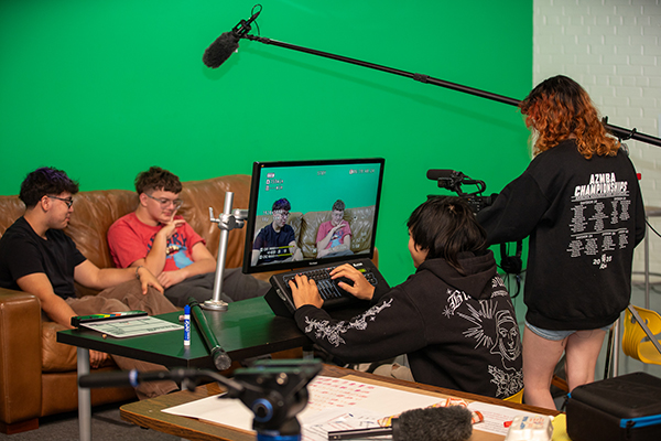 A teen boy and teen girl film and edit two teen boys talking on a couch